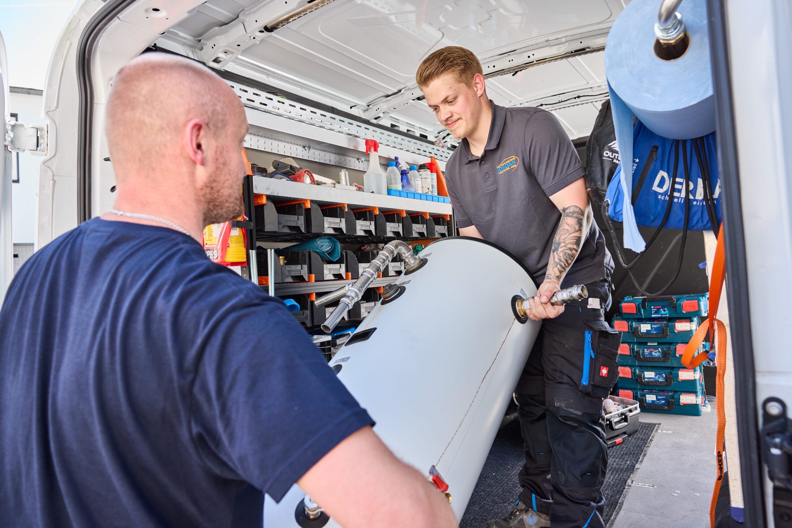Zwei Monteure verladen gemeinsam einen Warmwasserspeicher in ein Servicefahrzeug – Teamarbeit bei Jordan Haustechnik